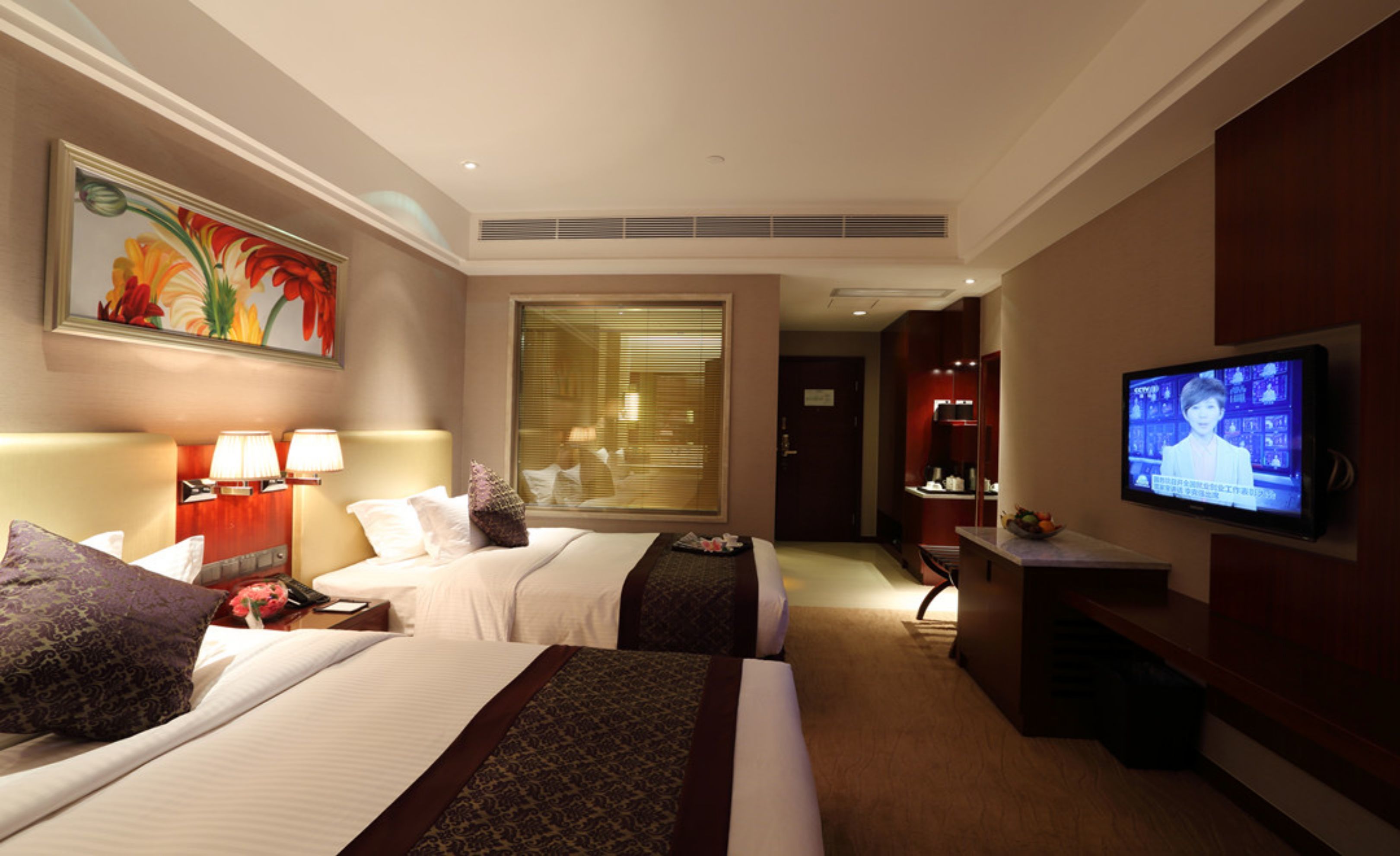 A hotel room with two beds, a television, a painting, and a window with blinds.