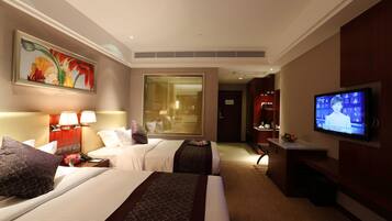 A hotel room with two beds, a television, a painting, and a window with blinds.