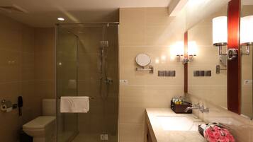 A modern bathroom with a glass-enclosed shower, a toilet, a sink with a mirror, and a vase of pink flowers.