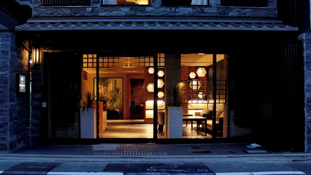 A hotel entrance with a traditional design, featuring a stone facade, large glass doors, and a well-lit interior with modern furnishings. - Kyoto Shinmachi Rokkaku Hotel grandereverie (Kyoto)