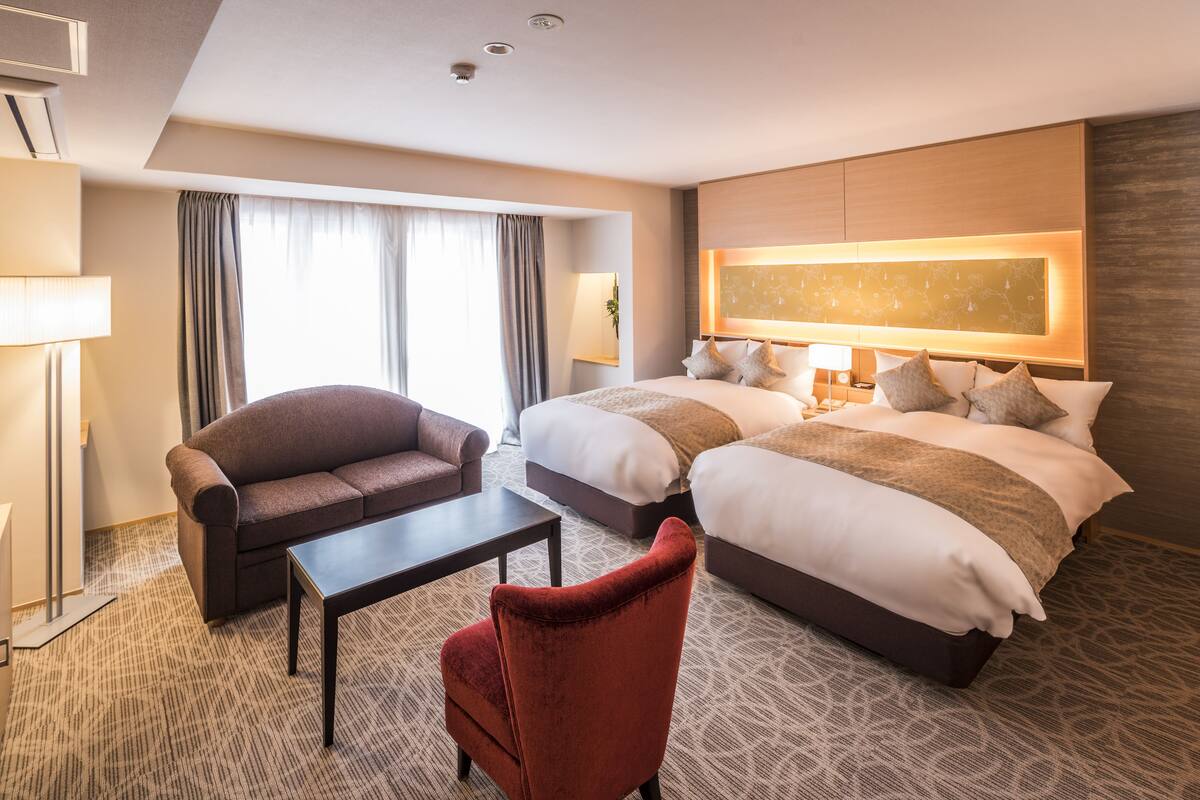 Ein Hotelzimmer mit zwei Betten, einem Sofa, einem Couchtisch und einer Lampe.