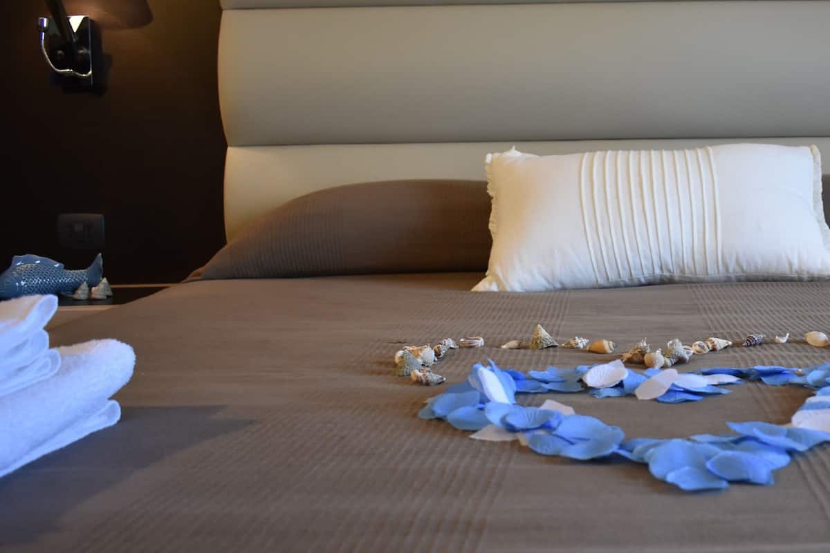 Un letto rifatto con cura, decorato con un composizione a forma di cuore di petali blu e conchiglie sul copripiumino.