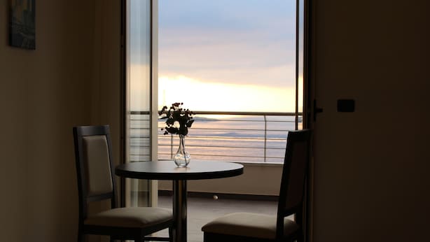 A room with a balcony, a table with a vase, and two chairs. - Miramare Scilla GYH Luxury (Scilla)