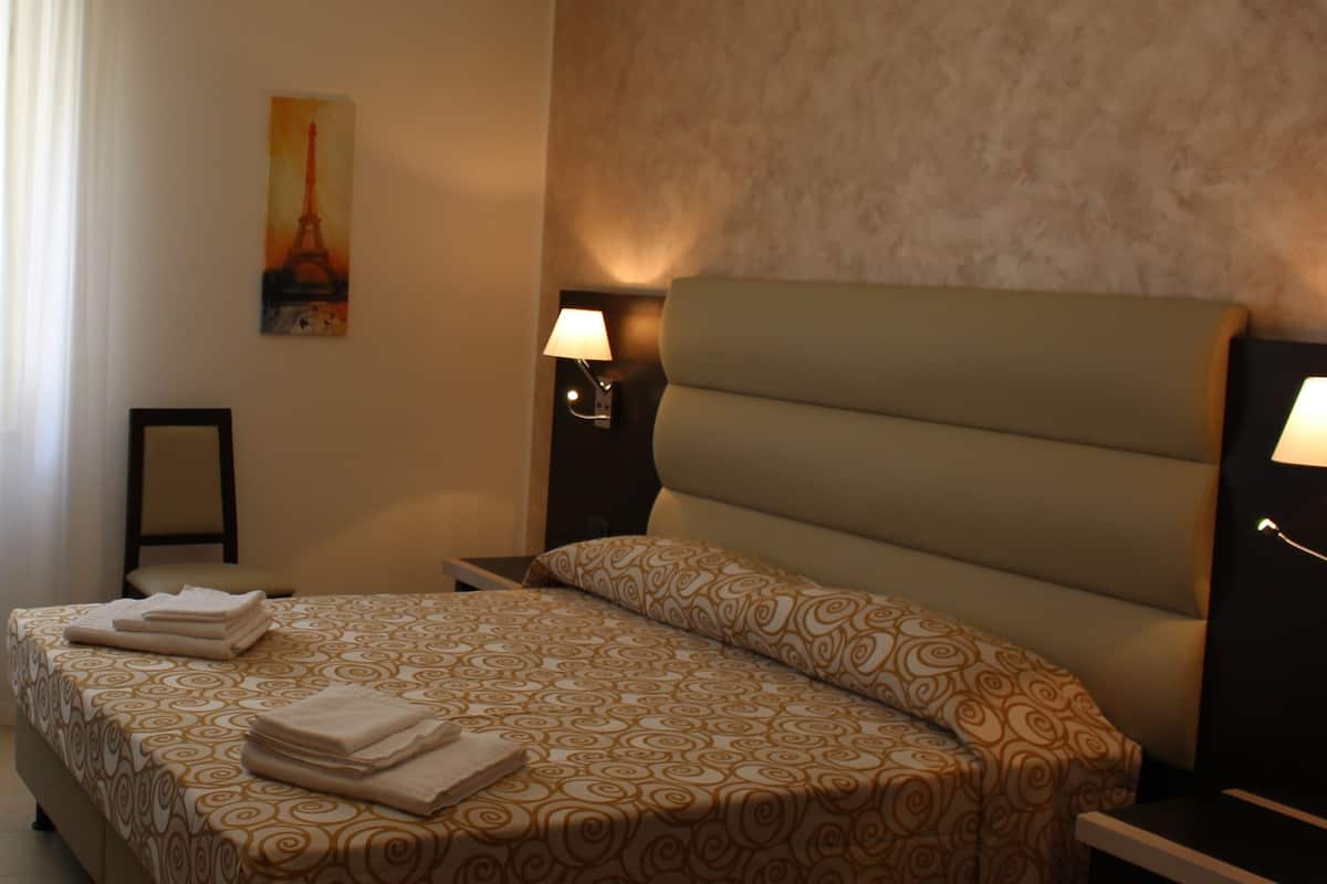 Una camera d'albergo con un letto, due comodini, una lampada, un quadro della Torre Eiffel e una finestra con tende.