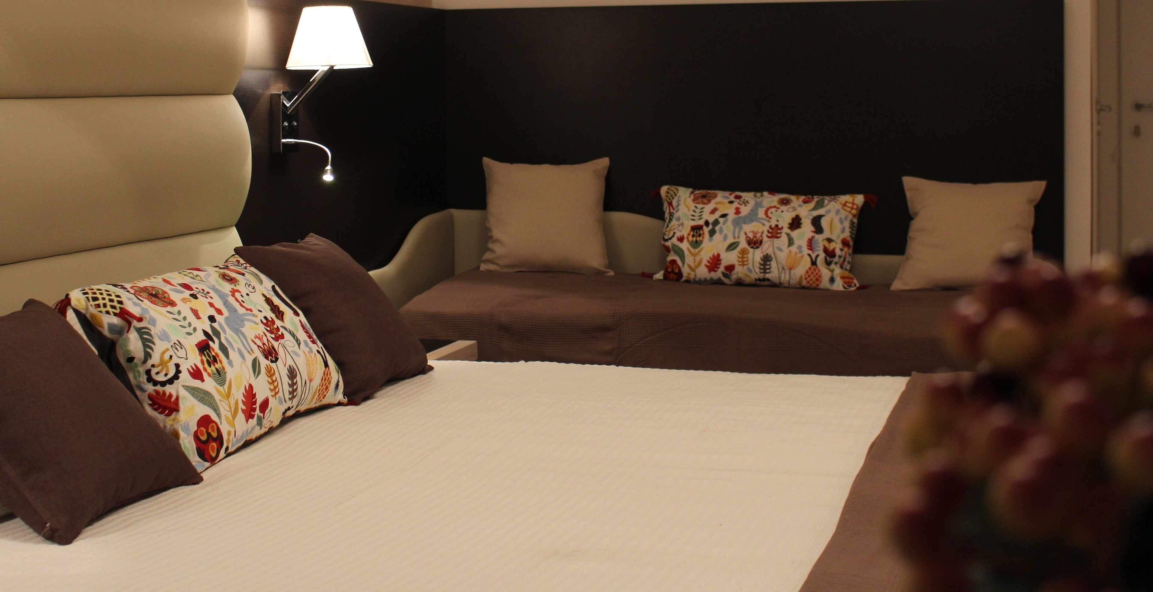 A hotel room with a large bed, two smaller beds, a nightstand with a lamp, and a dark headboard.