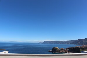 Vista costera con cielo azul despejado, costa rocosa y un edificio en un acantilado.