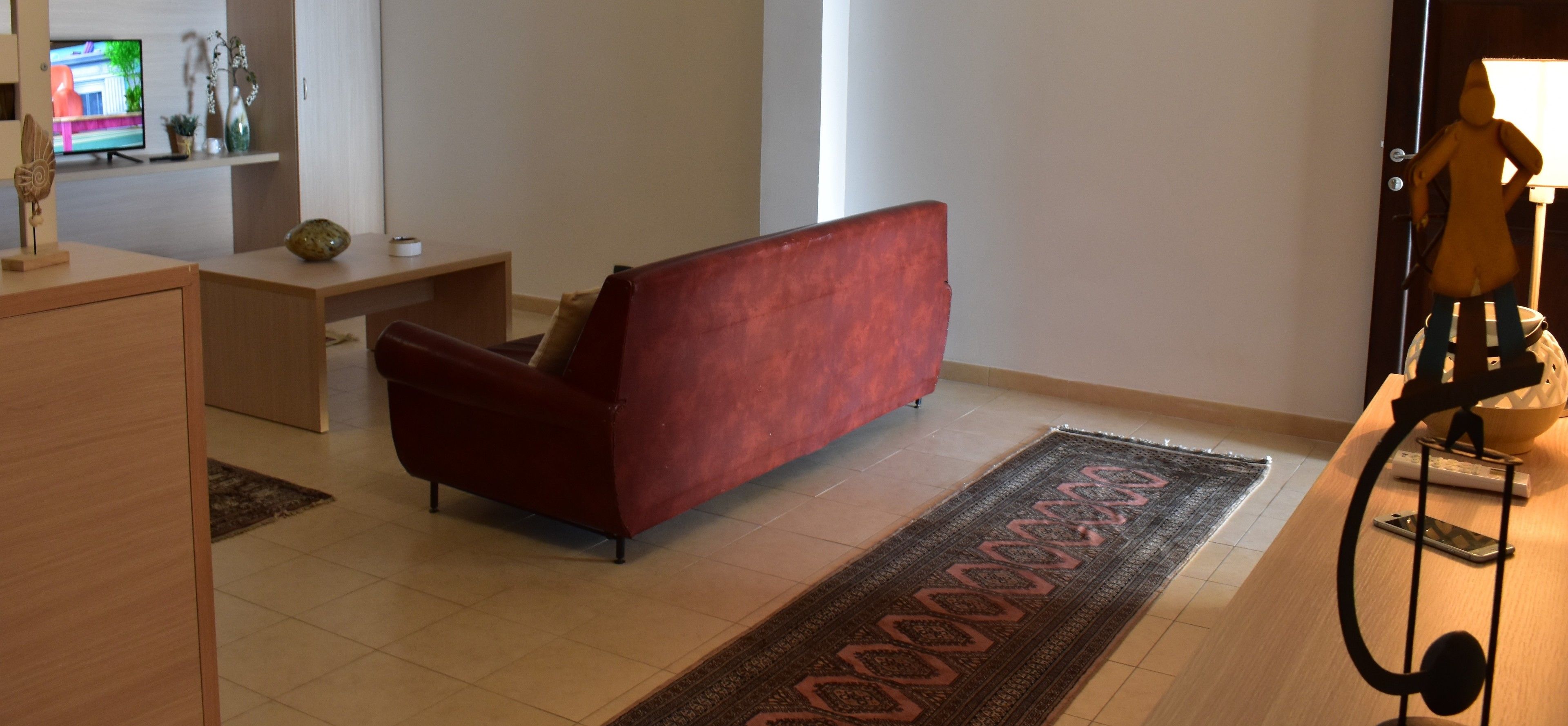 A living room with a red sofa, a wooden desk, a television, and a lamp.