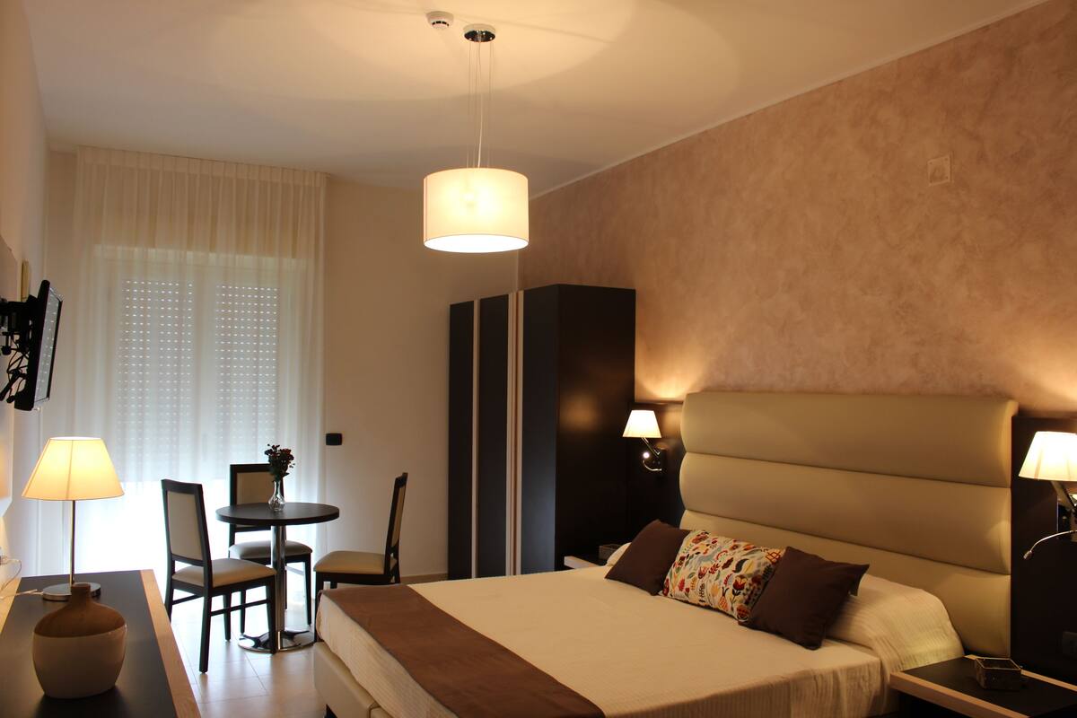 Camera d'albergo con un letto grande, una scrivania con sedia, un tavolino e una lampada.
