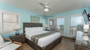 A bedroom with a bed, nightstands, a desk, a chair, and a ceiling fan. - Suntide II 301 - Oceanfront Condo, BBQ's, Sand Volleyball, Sun Deck, Beachfront Pool & Spa (South Padre Island)