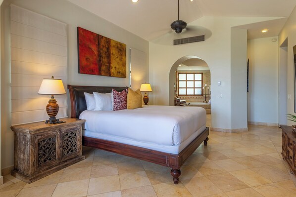 A spacious bedroom with a large bed, two bedside tables with lamps, a decorative headboard, and a large painting above the bed.