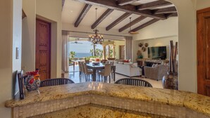 Una cocina con encimera de mármol, vigas de techo de madera y un comedor con vista al océano.