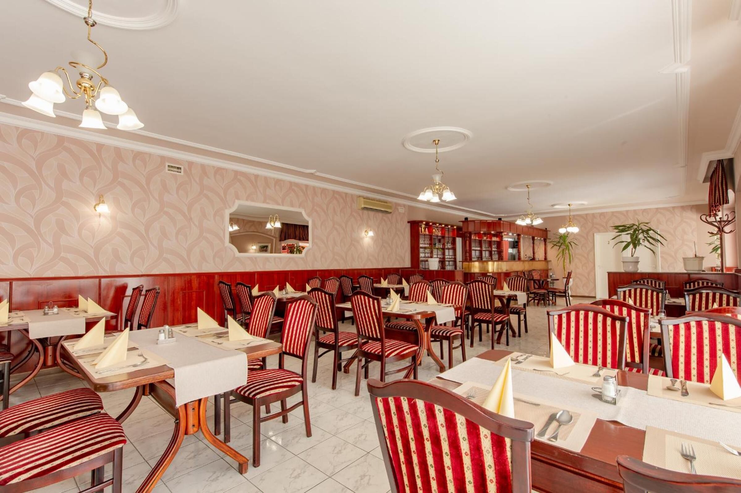 Un restaurant amb taules rodones i cadires a ratlles, una zona de bar i un mirall a la paret.