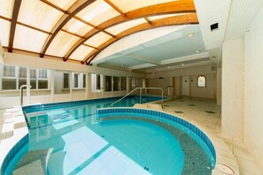 An indoor swimming pool with a curved design, wooden ceiling beams, and tiled walls. - Aqua Blue Hotel (Hajduszoboszlo)