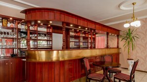 Una zona de bar con una barra de madera curva, varias estanterías con cristalería y una mesa redonda con sillas.