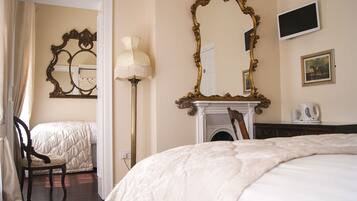 A hotel room with a large bed, a sitting area with a chair, a fireplace, and two ornate mirrors.