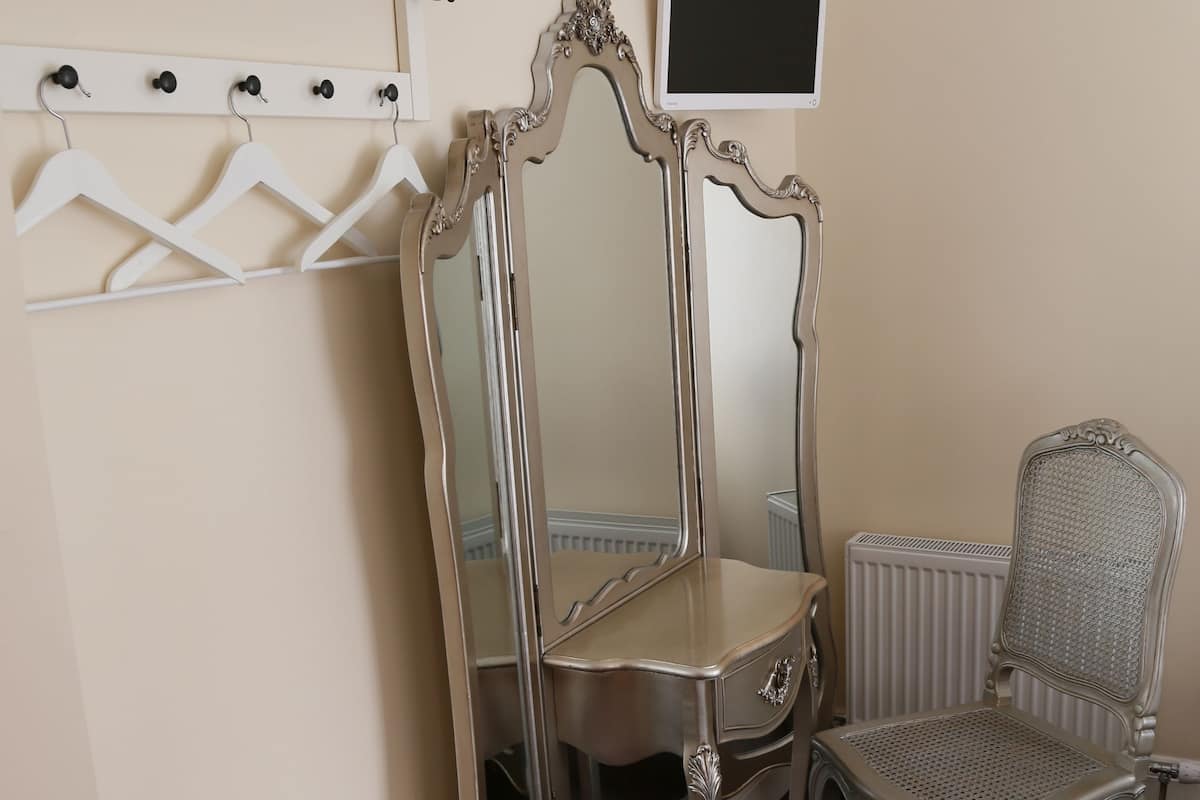 Ein Zimmer mit Schminktisch, Spiegel, Stuhl und Heizkörper.