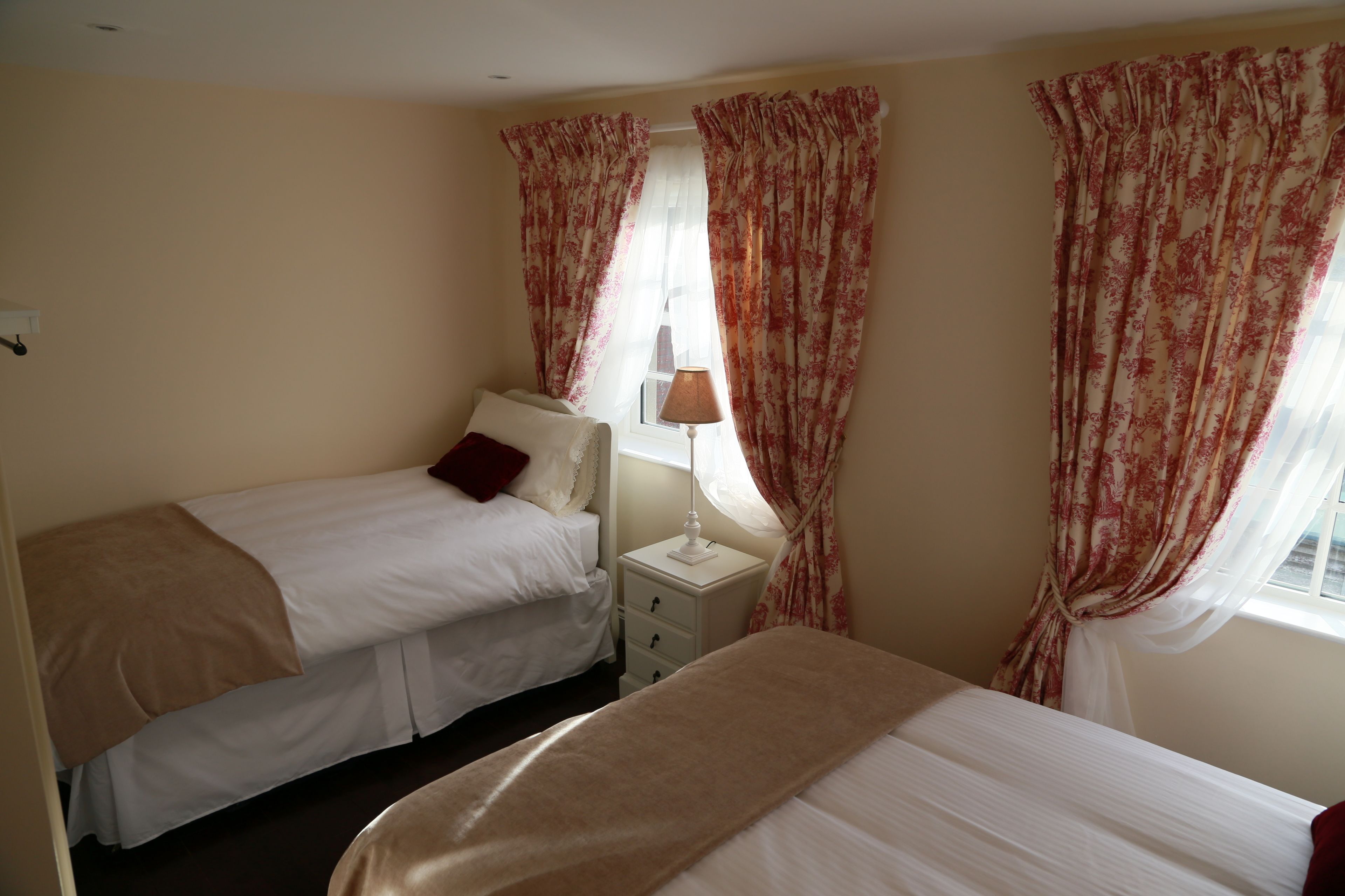 Habitación de hotel con dos camas, una mesita de noche con lámpara y cortinas con motivos florales.