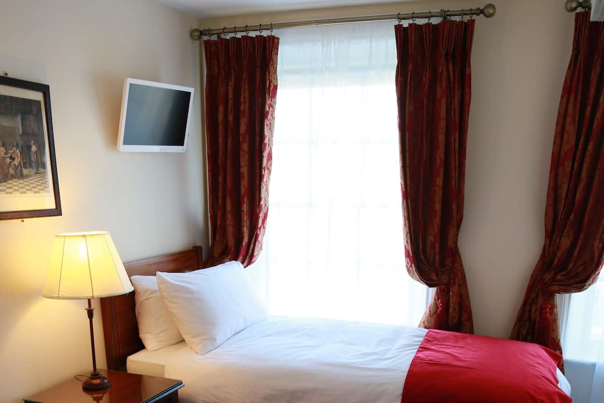 Ein Hotelzimmer mit zwei Betten, einem Nachttisch mit Lampe, einem Flachbildfernseher und roten Vorhängen.