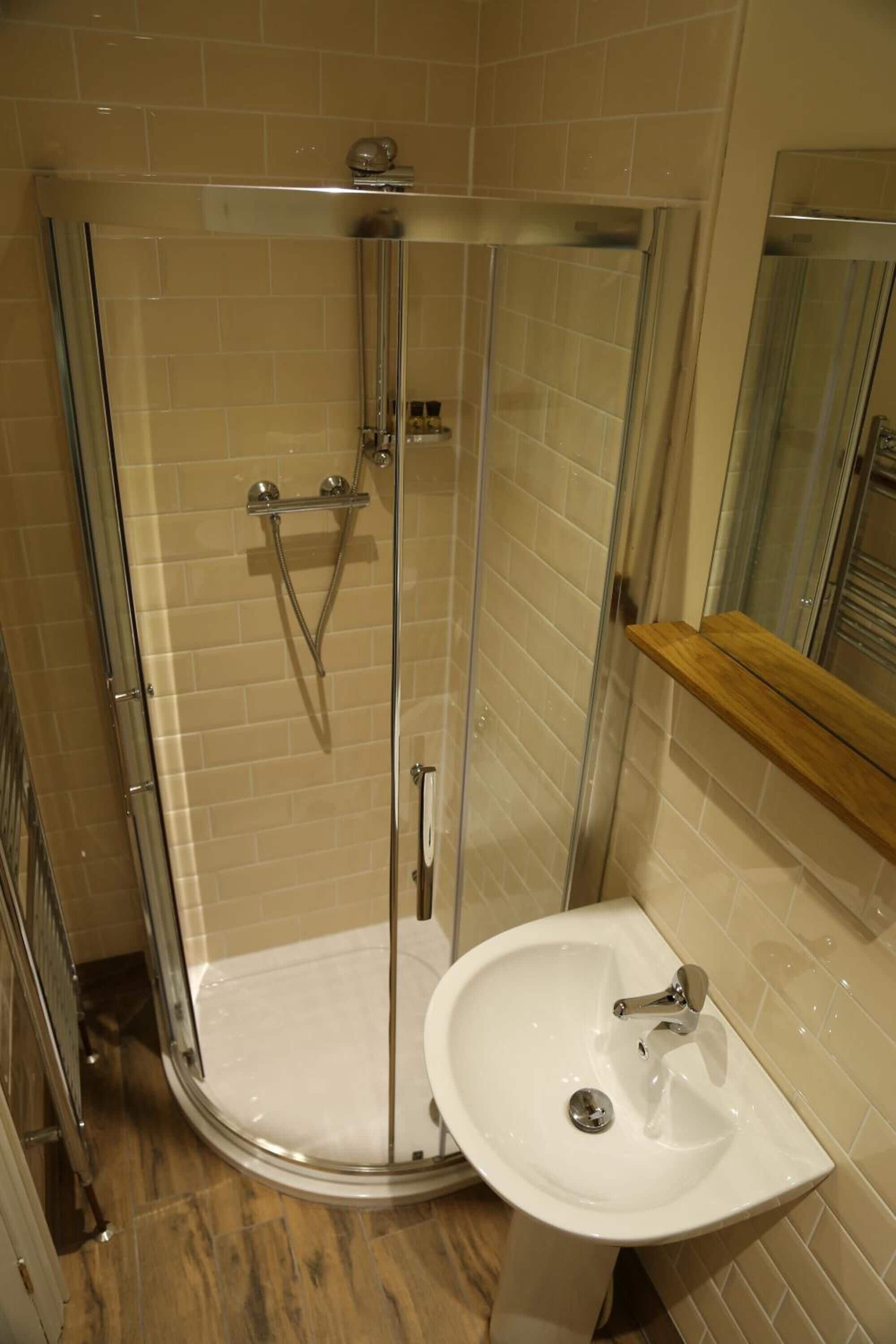 Eine Dusche mit Glastür, ein Waschbecken und ein Holzregal.
