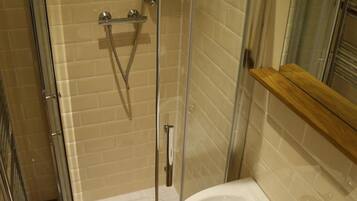 Eine Dusche mit Glastür, ein Waschbecken und ein Holzregal.
