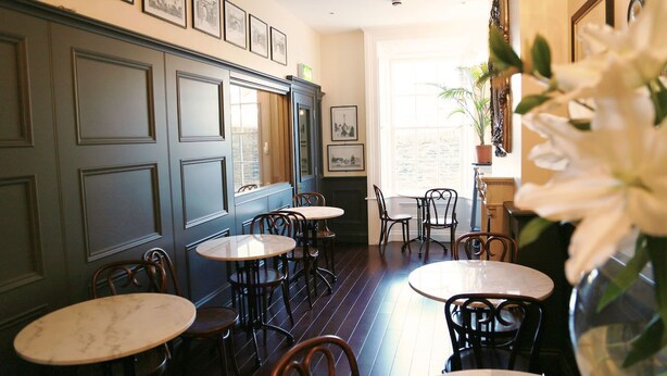 A dining area with round tables and chairs, framed pictures on the wall, and a window with natural light. - Number 8 The Townhouse (Londonderry)