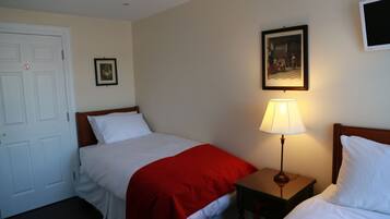A hotel room with two single beds, a nightstand with a lamp, a door with a no entry sign, and a framed picture on the wall.