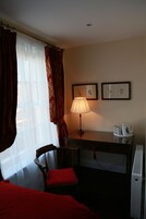Habitación de hotel con cama, escritorio con lámpara, una silla y dos cuadros en la pared.
