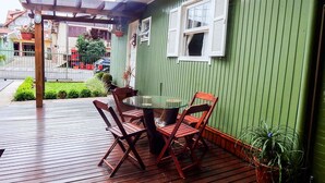 A green house with a wooden deck, a glass table, and two wooden chairs. - Residencial Vista do Centro Gramado (Gramado)