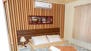 A bedroom with a wooden headboard, a bed with a floral bedspread, a nightstand with a lamp, and a wall-mounted air conditioner. - Residencial Vista do Centro Gramado (Gramado)
