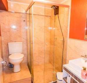 Un baño con ducha envuelta en vidrio, inodoro y lavabo con espejo.