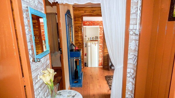 A narrow hallway with a wooden floor, a small table with a vase of flowers, and a blue cabinet. - Residencial Vista do Centro Gramado (Gramado)