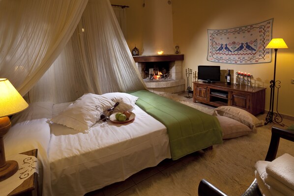 Un dormitorio con cama, una mesita de noche con lámpara, televisor, chimenea y un tapiz en la pared.