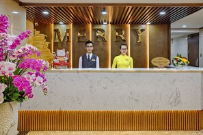 A reception desk with a 'MERRY' sign, a receptionist, and a receptionist's desk. - Merry Hotel (Da Nang)