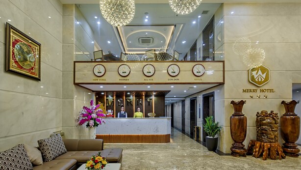 A hotel reception area with a marble floor, a reception desk, a sofa, and a coffee table with flowers. - Merry Hotel (Da Nang)