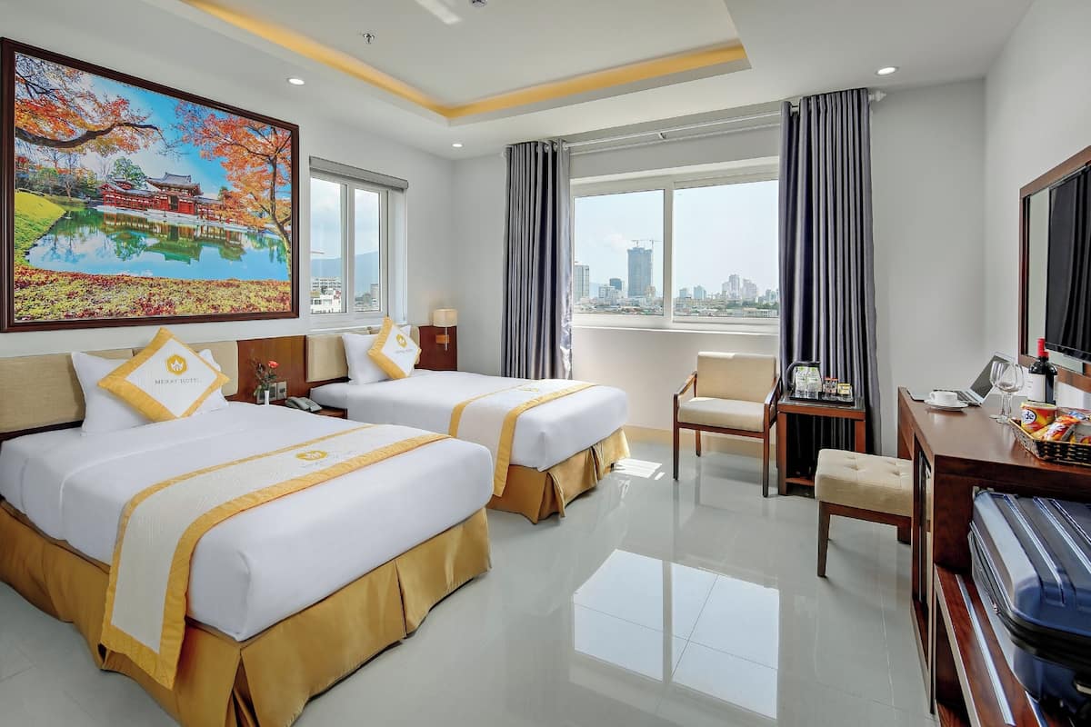 A hotel room with two beds, a desk with a laptop, a chair, a large window with a city view, and a painting on the wall.