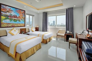A hotel room with two beds, a desk with a laptop, a chair, a large window with a city view, and a painting on the wall. - Merry Hotel (Da Nang)