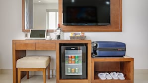 A compact hotel room with a wooden desk, a laptop, a minibar, a television, a small refrigerator, a suitcase, slippers, and a mirror. - Merry Hotel (Da Nang)