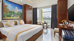 A hotel room with a large bed, a desk, a chair, a TV, and a painting of a castle. - Merry Hotel (Da Nang)