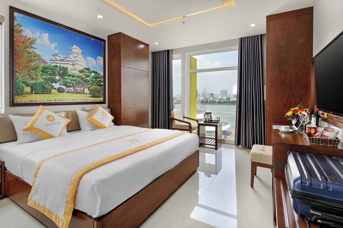 A hotel room with a large bed, a desk, a chair, a TV, and a painting of a castle.