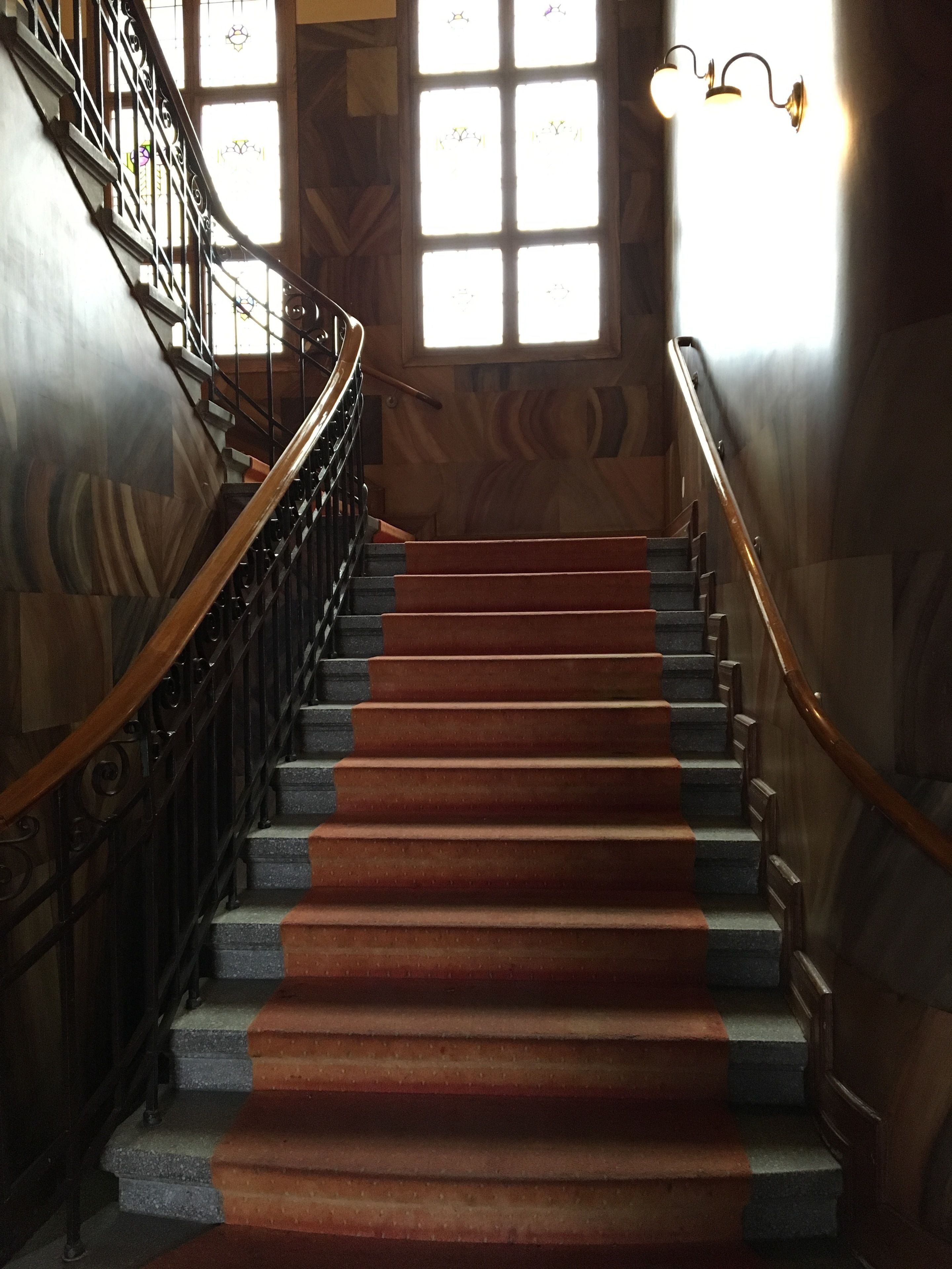 A grand staircase with a red carpet, black balustrade, and a wooden handrail.