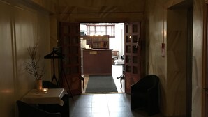 A hallway with a chandelier, a reception desk, and a view into a room with a bed and a window.