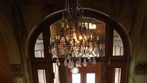 An arched doorway leading to a room with a chandelier, wooden doors, and a checkered floor.