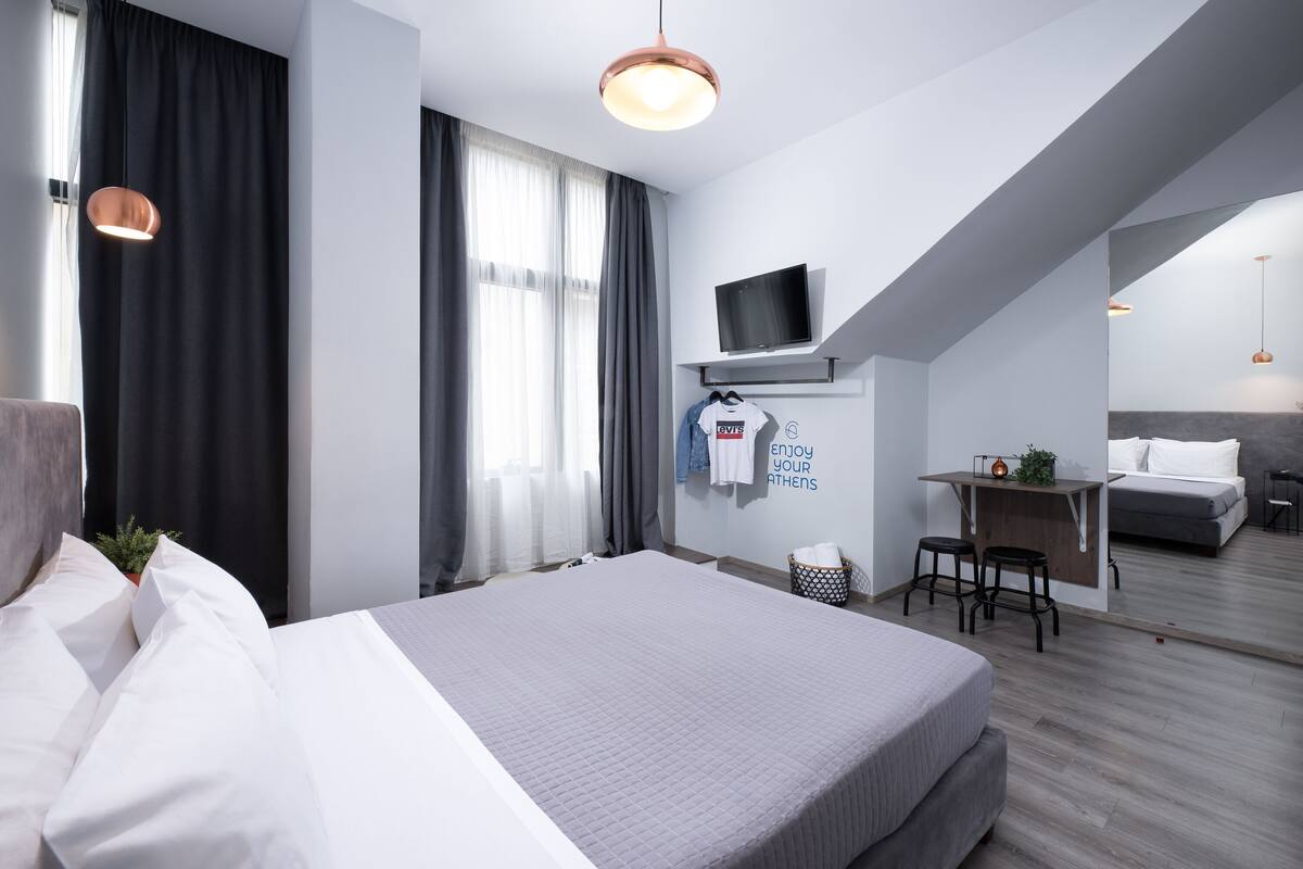 Ein modernes Hotelzimmer mit einem großen Bett, einem Schreibtisch mit Stuhl, einem Fernseher und einem kleinen Balkon.