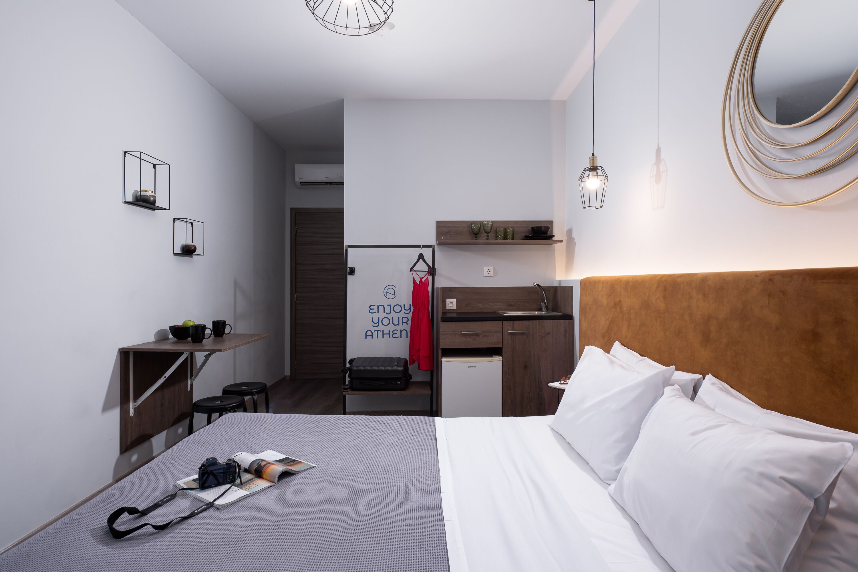 A modern hotel room with a bed, bedside table, and a small kitchenette.
