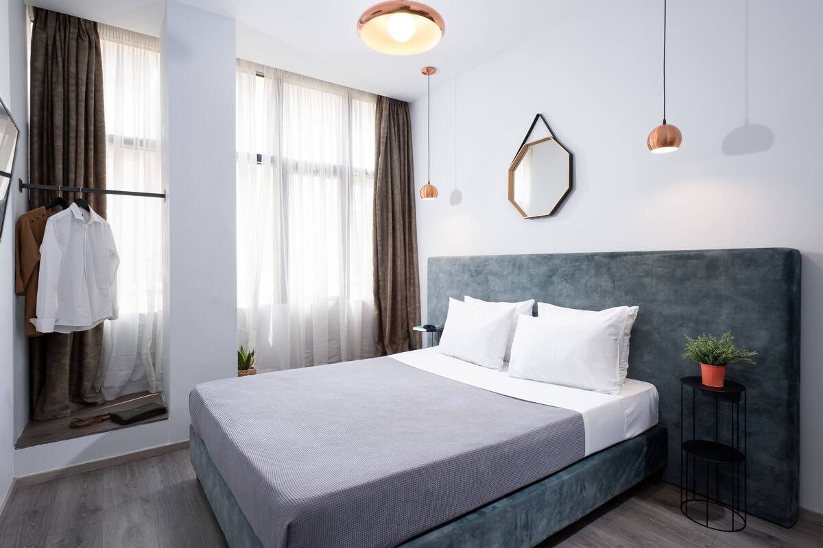 Ein modernes Schlafzimmer mit einem großen Bett, einem Kopfteil, einem Nachttisch, einem Spiegel und einer Hängeleuchte.