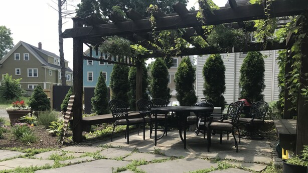 Une terrasse carrelée, une pergola en bois et du mobilier d’extérieur.