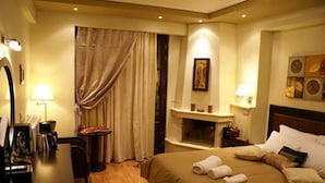 Quarto de hotel com uma cama, escrivaninha, cadeira, lareira e espelho.