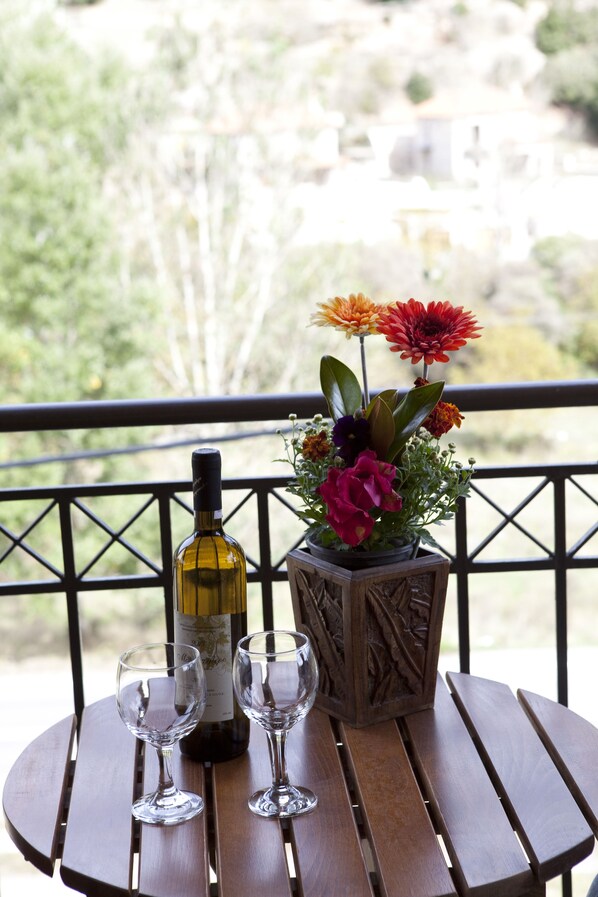 A wooden table with a bottle of wine and two glasses on a balcony with a railing. - Kaloneri Rooms (Gortynia)