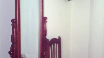 A room with a wooden chair, a wooden wardrobe, and a television mounted on the wall.