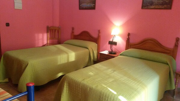 Quarto com duas camas de solteiro, uma mesa de cabeceira com abajur e uma pequena mesa com uma cadeira.